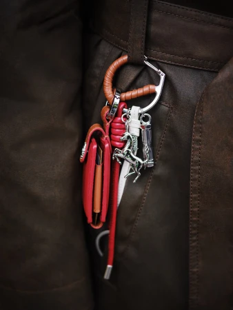 Close-up of a brown leather jacket with a wallet, carabiner, and charms hanging from a belt loop, fashion detail.