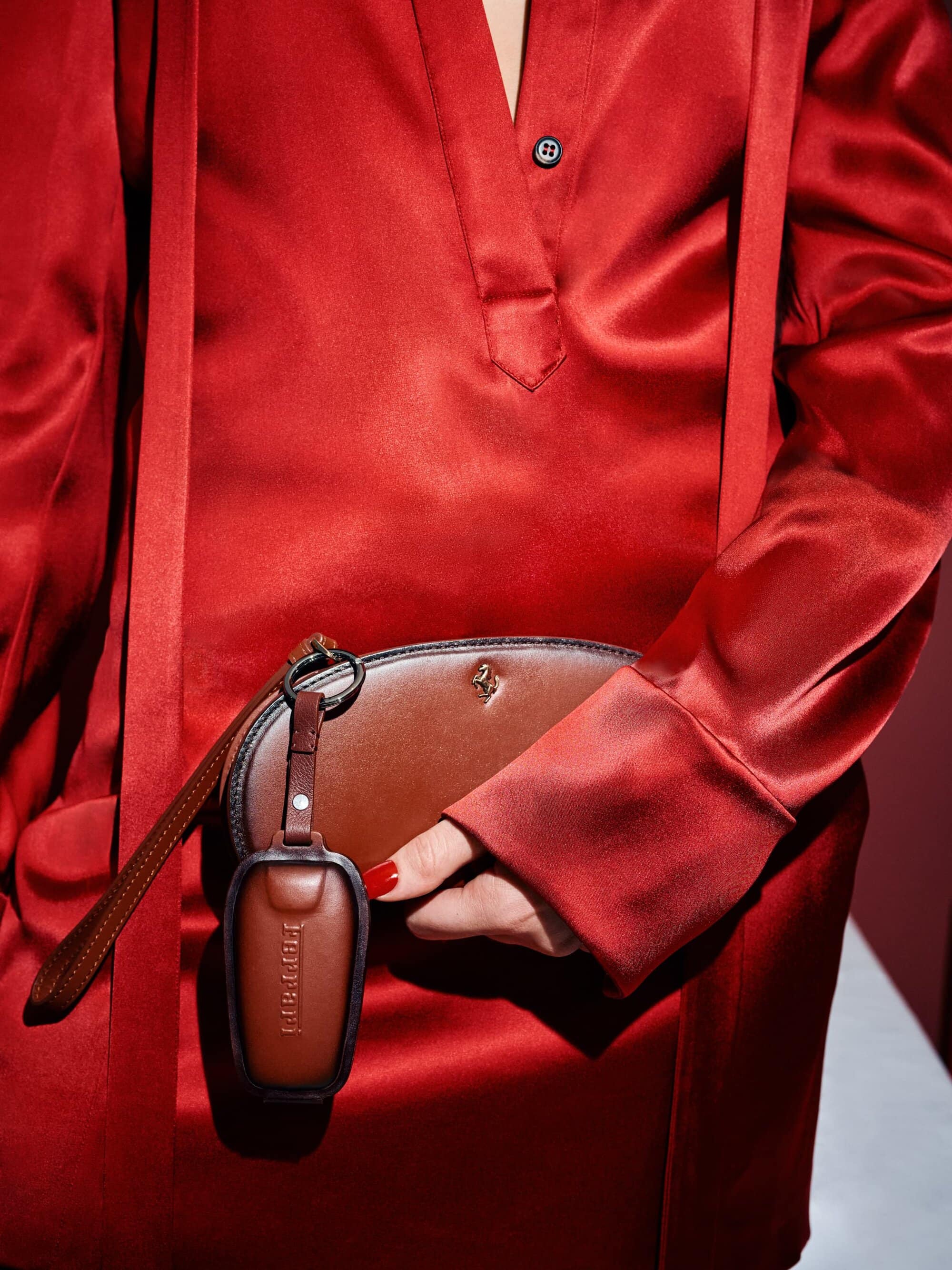 Close-up of a woman wearing a red satin dress and holding a brown leather pouch and key fob, highlighting fashion and luxury.