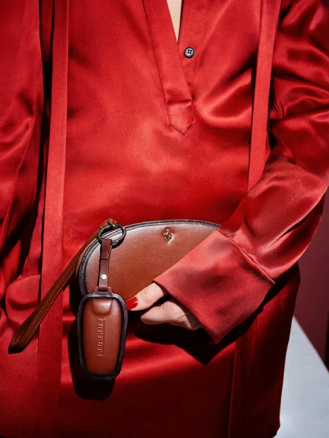 Close-up of a woman wearing a red satin dress and holding a brown leather pouch and key fob, highlighting fashion and luxury.