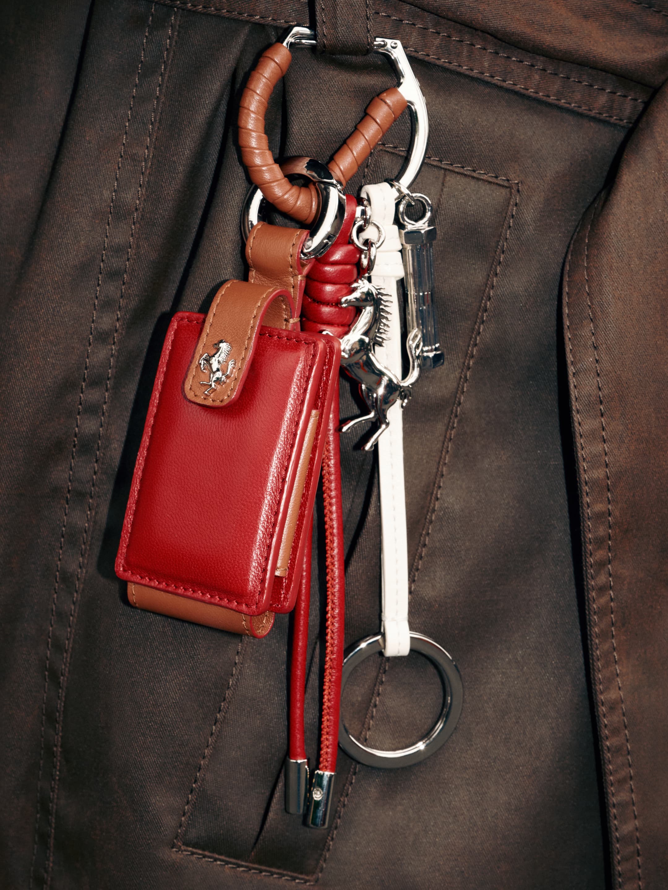 Close-up of a brown leather jacket with a hanging red leather accessory, leather strap, and metal keychain.