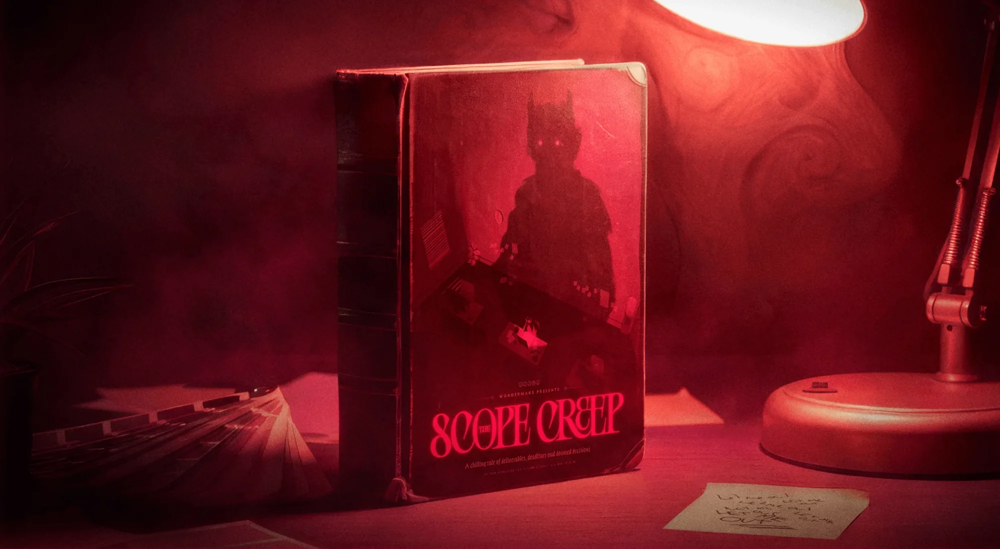 A horror book titled "Scope Creep" stands upright on a desk, illuminated by a lamp, with a spooky figure on its cover, in a red-lit room.