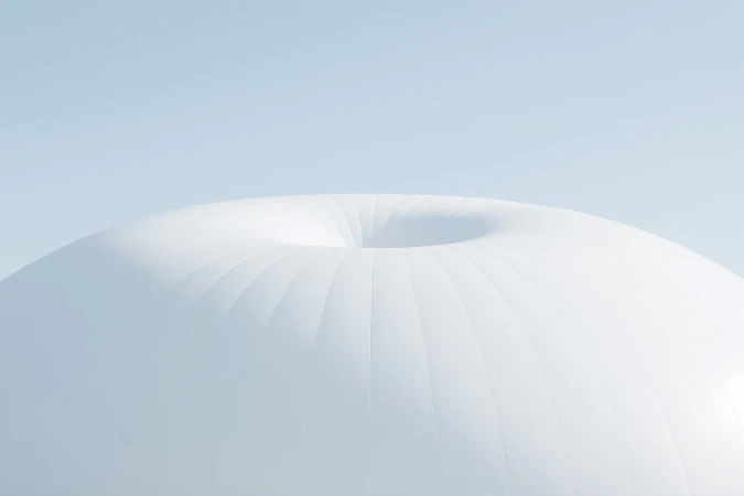 Minimalist architectural shot featuring a smooth, white dome structure against a pale blue sky, creating a clean and modern aesthetic.