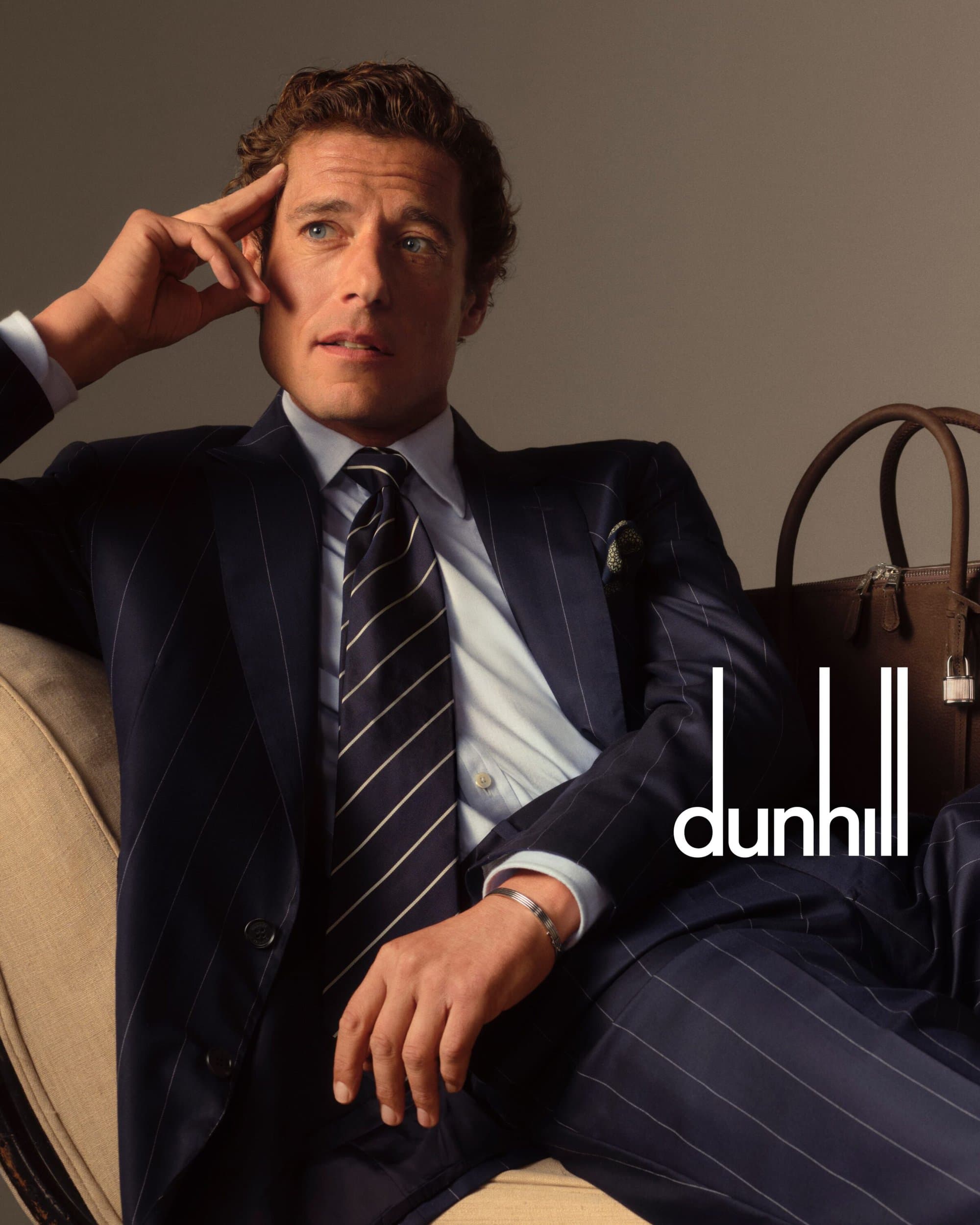 Portrait of an adult man wearing a dark pinstripe suit and striped tie, reclining in an armchair with a briefcase in the background.