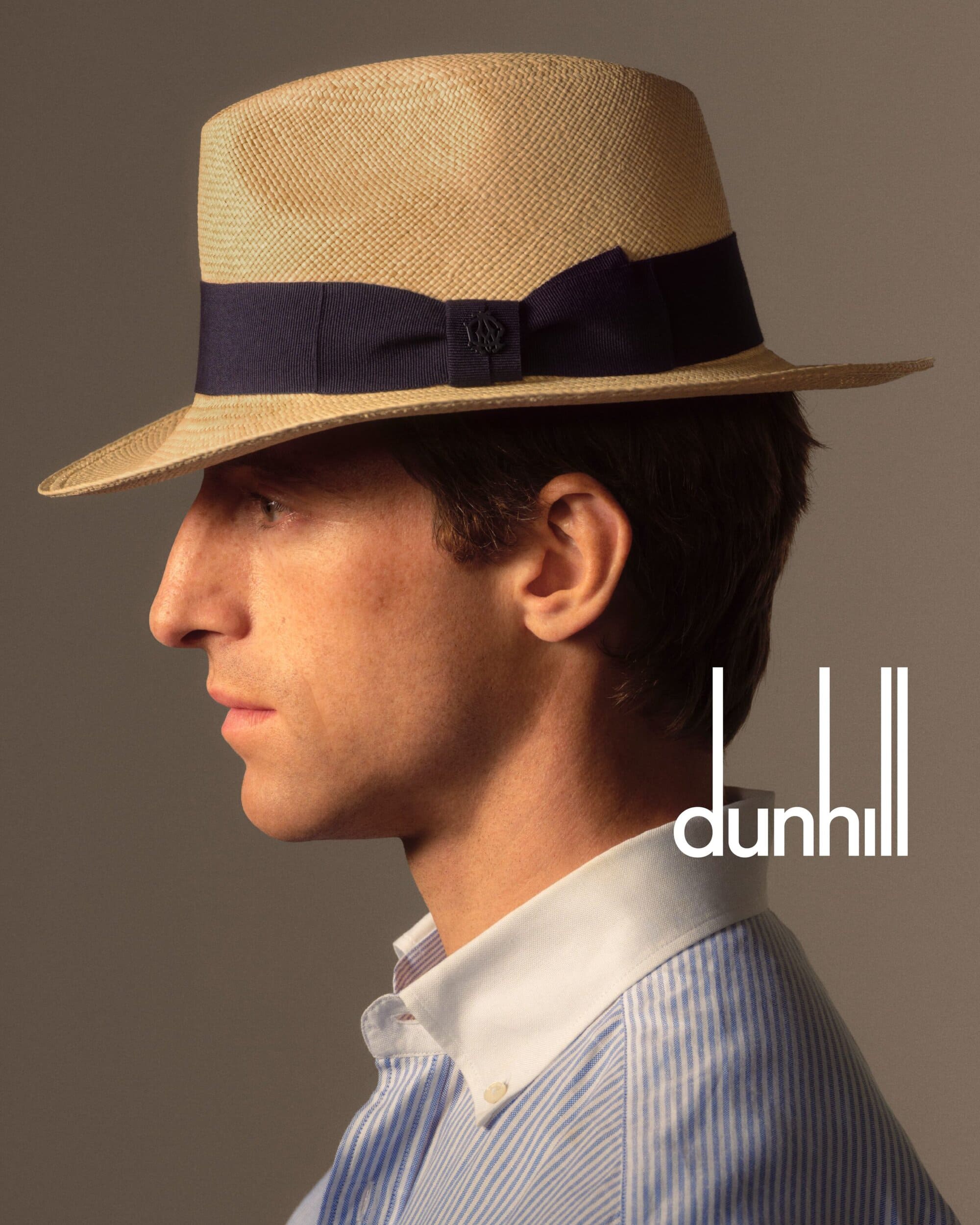 Side profile studio shot of a fair-skinned male wearing a straw hat with a navy band and a striped shirt and white collar.
