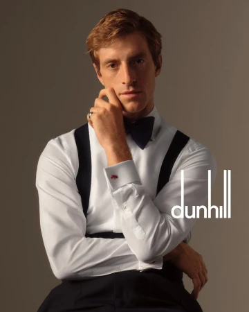 Portrait of a blond male model in formal wear and suspenders, gazing at the camera, with the Dunhill logo visible.