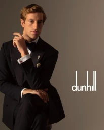Man wearing a black suit and bow tie posing against a neutral grey studio backdrop for Dunhill Spring 2026 Ad Campaign
