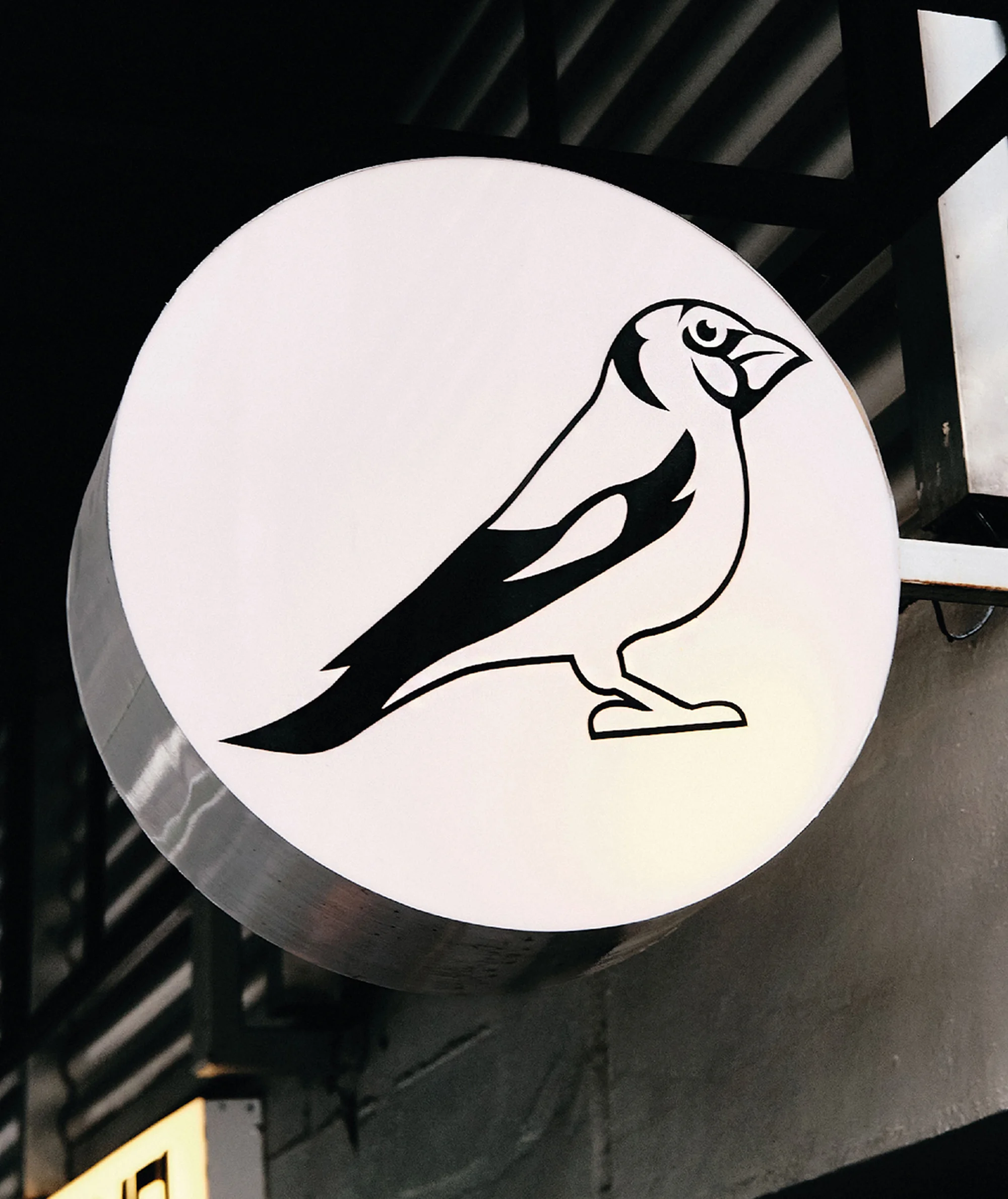 Close-up of a round, white sign featuring a black line drawing of a bird, mounted on a dark gray wall, creating a high-contrast graphic.