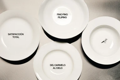 Four white ceramic plates arranged from above on a metallic surface, featuring black typography and a small bird illustration.