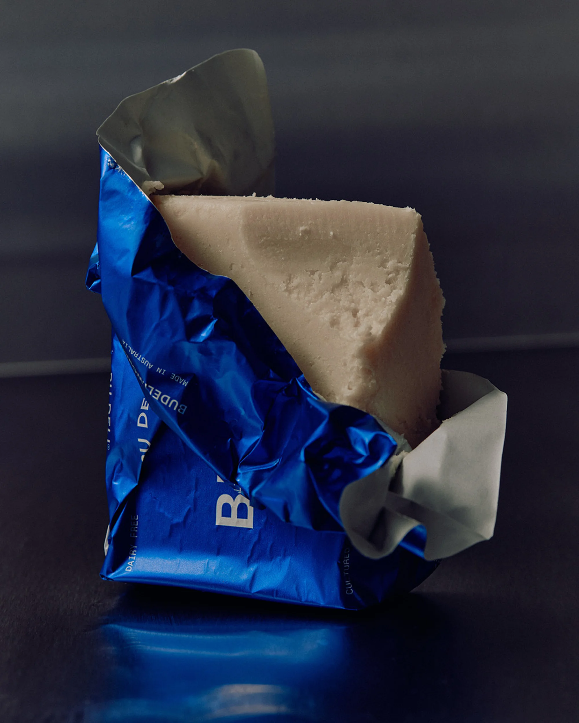 Wrapped block of white cheese in crinkled blue packaging, studio lighting, close-up food photography for food and beverage use.