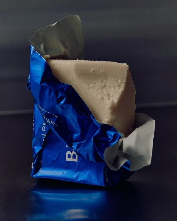 Wrapped block of white cheese in crinkled blue packaging, studio lighting, close-up food photography for food and beverage use.