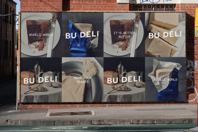 Outdoor billboard ad for Bu Deli butter featuring slices of butter, chocolate cake, and bread in a tiled display on brick wall.