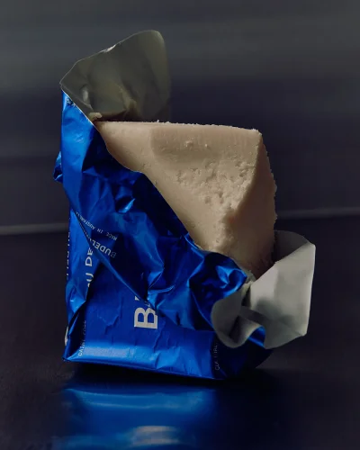 Unwrapped blue foil food packaging revealing a block of off-white solid food against a dark reflective surface