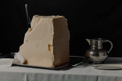 Large block of butter with a knife stuck in it on a silver tray alongside a metal pitcher and plate