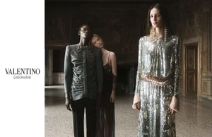 Three models posing in a grand historic interior for Valentino, featuring a metallic sequin dress and tailored garments.