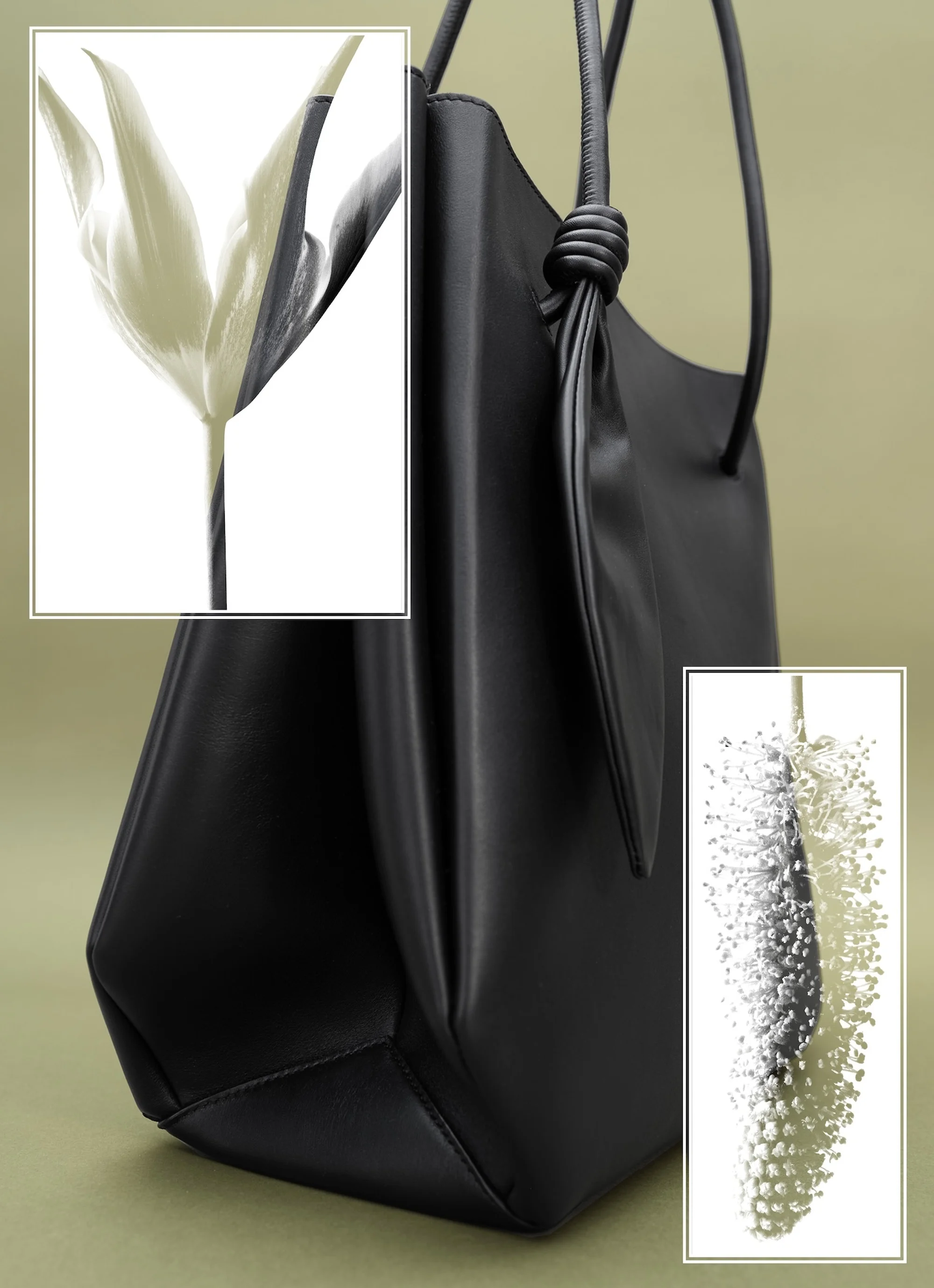 Studio shot of a black leather tote bag with handle knot detail, next to white and spotted plants, against an olive background.