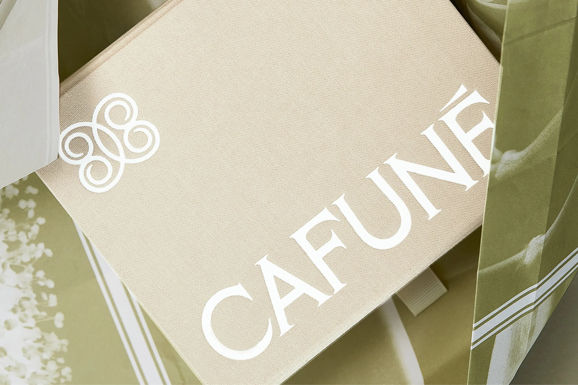 Close-up of a cream-colored Cafune branded gift box with white logo, nestled inside a striped cream and green shopping bag.