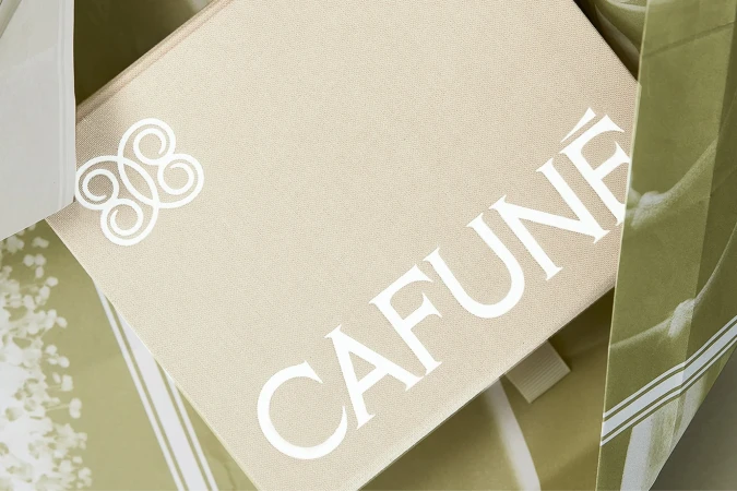 Close-up of a cream-colored Cafune branded gift box with white logo, nestled inside a striped cream and green shopping bag.