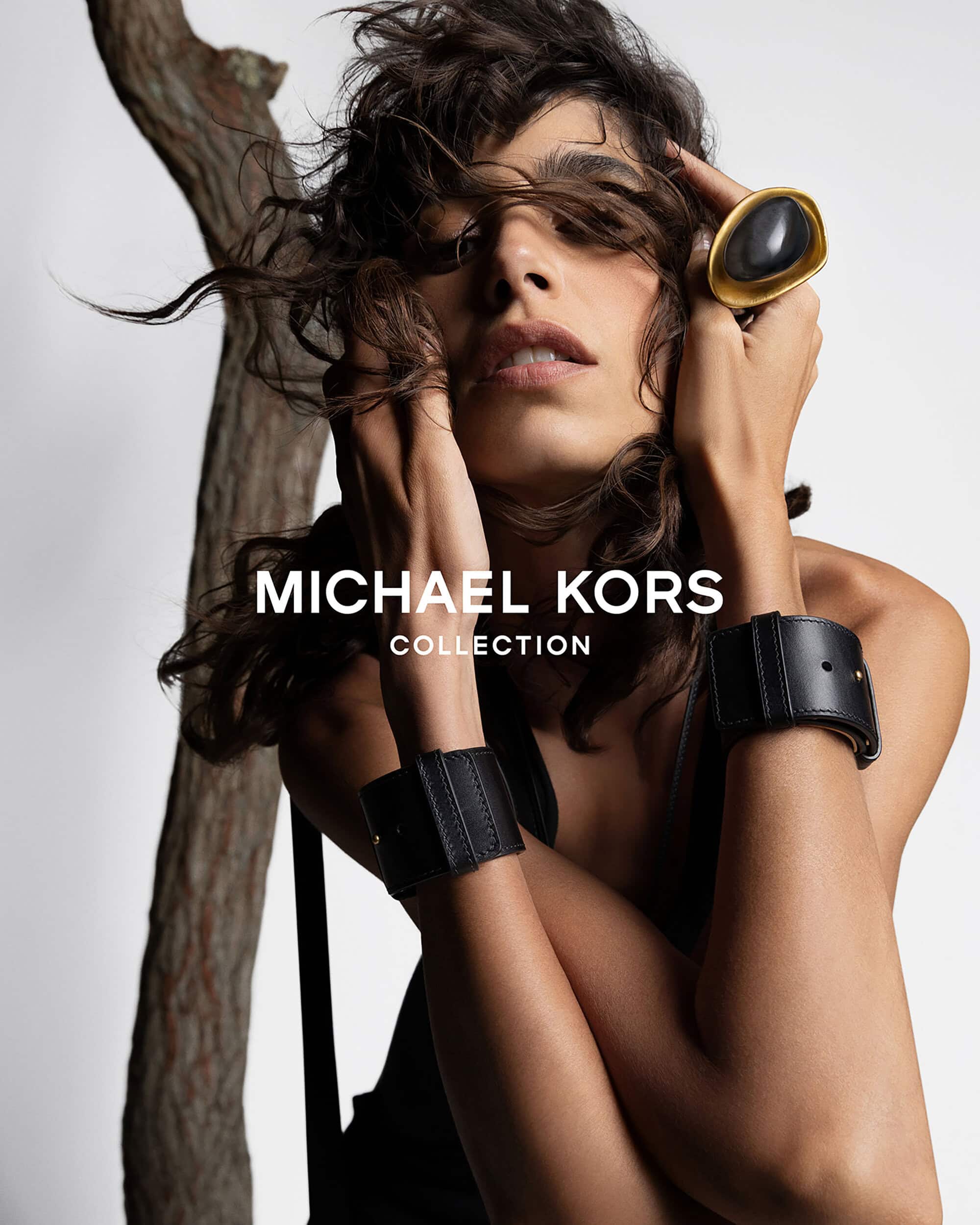 Portrait of a brunette female model wearing a ring and cuffs in a studio, showcasing fashion accessories with a branch backdrop.