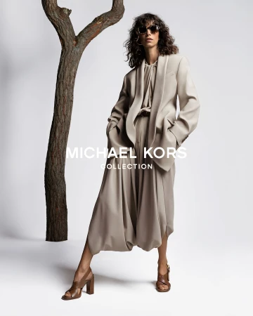 Model Mica Argañaraz wearing a tailored beige suit and sunglasses in a studio ad campaign featuring a stylized tree prop.