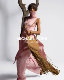Model Mica Argañaraz in pink knitted top and trousers holding a tan fringed handbag against a white studio background.