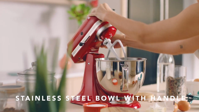 Red stand mixer with a stainless steel bowl and beaters is in use by a person on a white kitchen countertop.