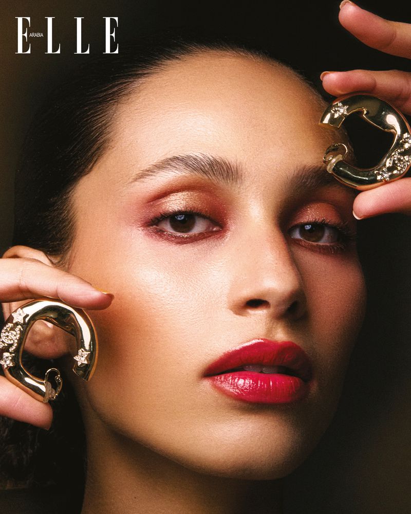 Close-up of woman with makeup and gold earrings, posing in front of dark backdrop, magazine cover with 'ELLE' title in the upper-left corner.