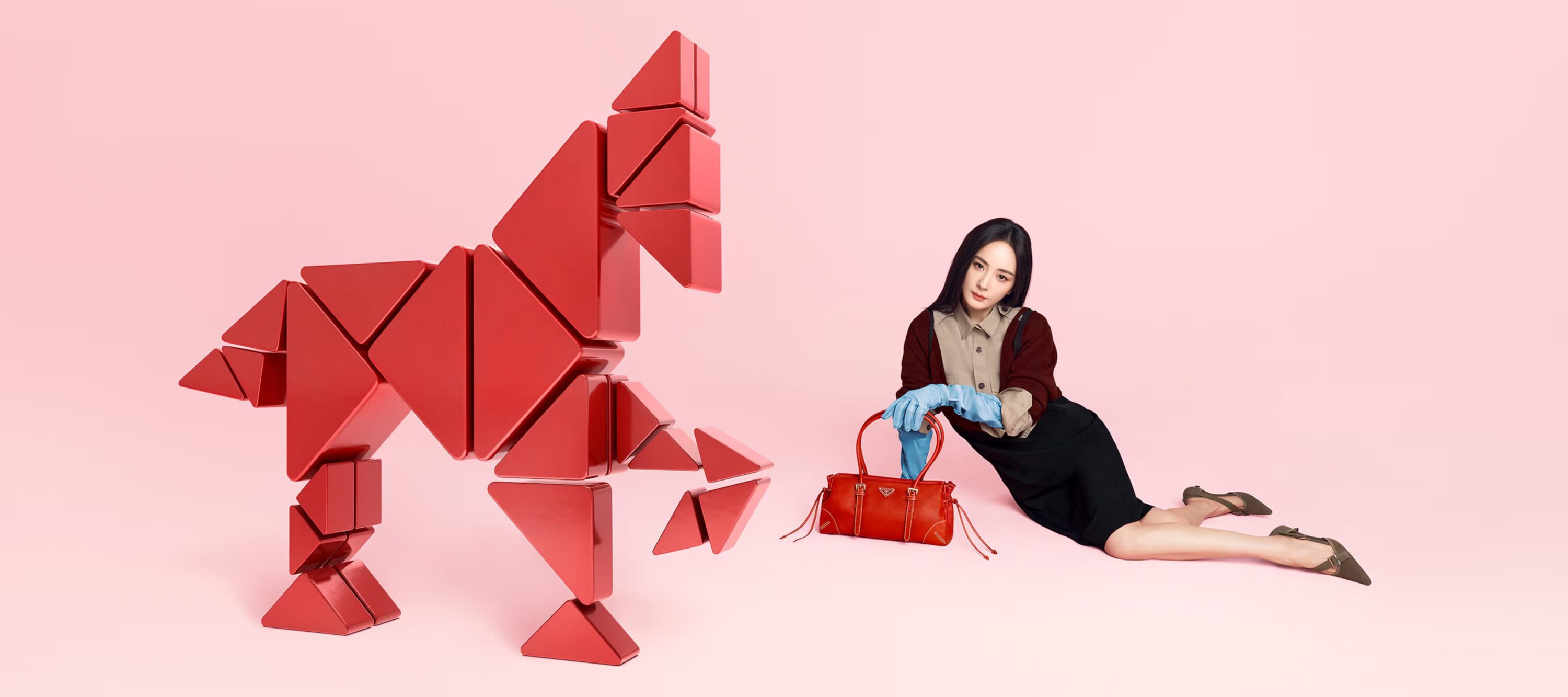 Fashion shot featuring an Asian woman lying next to a red triangular block sculpture, set against a pink background with a red purse.