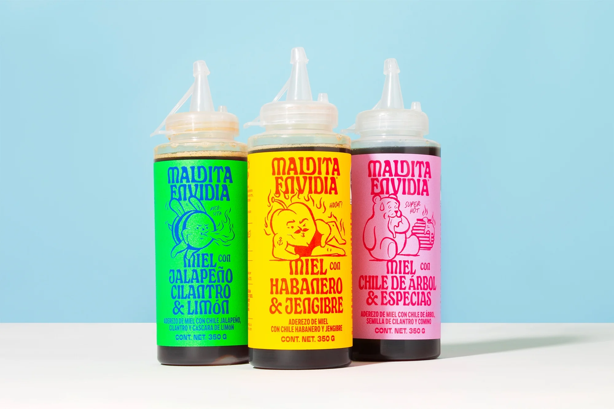Three colorful bottles of hot honey in green, yellow, and pink, with cartoon illustrations, against a light blue background.