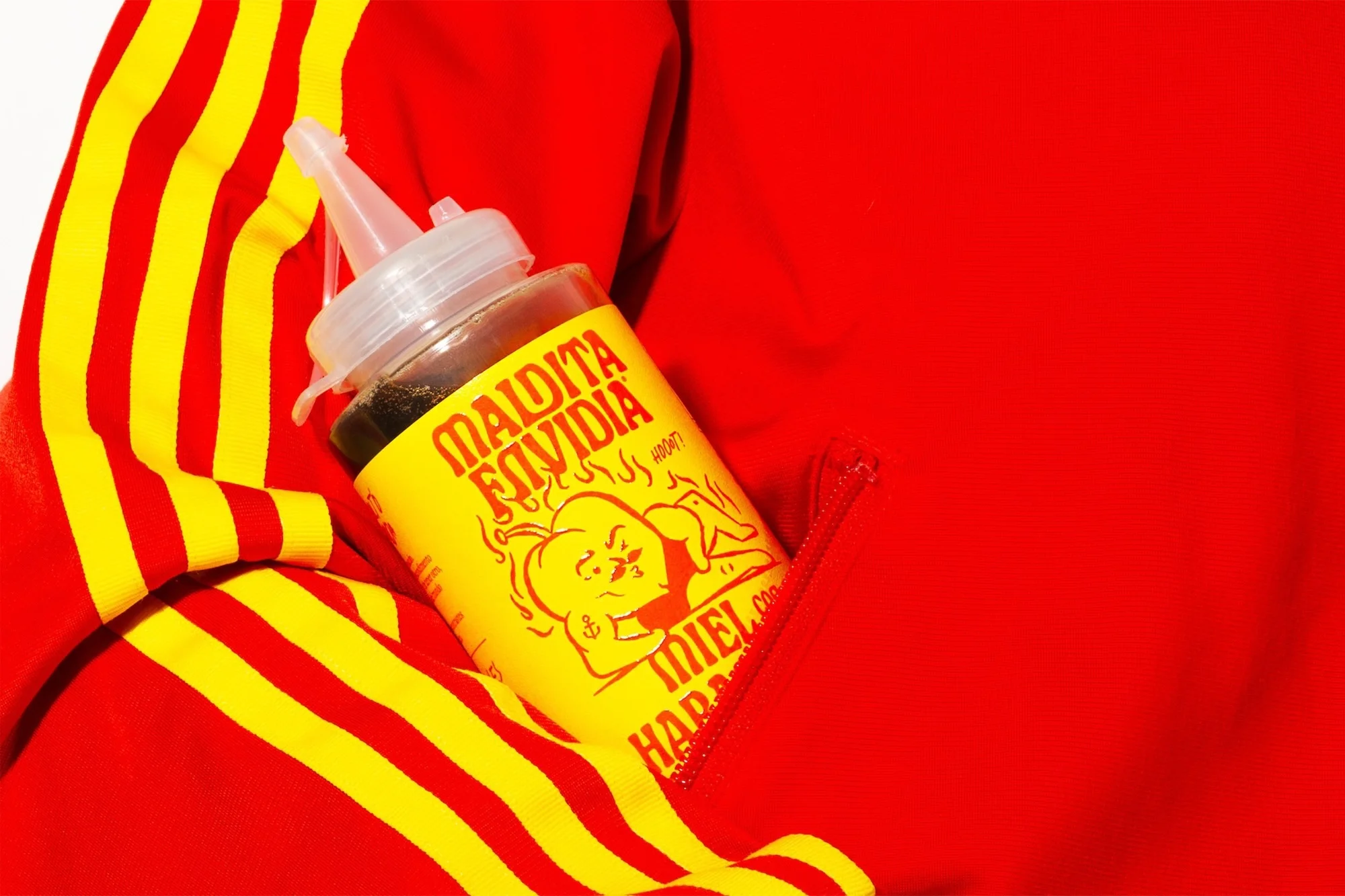 A squeeze bottle of honey with an illustrated label is nestled inside a red jacket with bright yellow stripes, in a bright, studio setting.