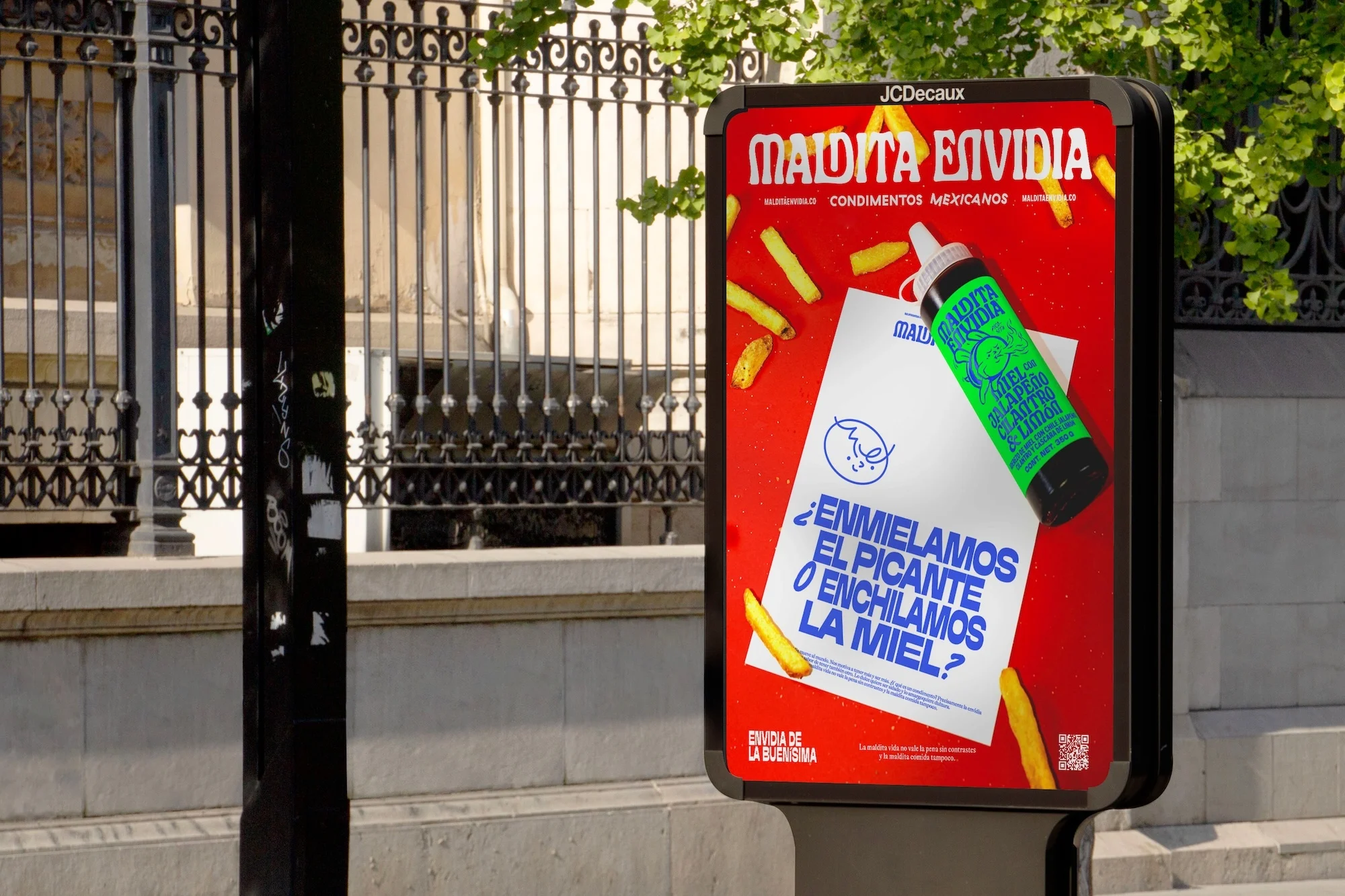 Outdoor advertising display showcasing a vibrant ad for Maldita Envidia Mexican condiments, featuring a sauce bottle and French fries graphics.