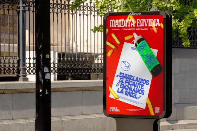 Outdoor advertising display showcasing a vibrant ad for Maldita Envidia Mexican condiments, featuring a sauce bottle and French fries graphics.