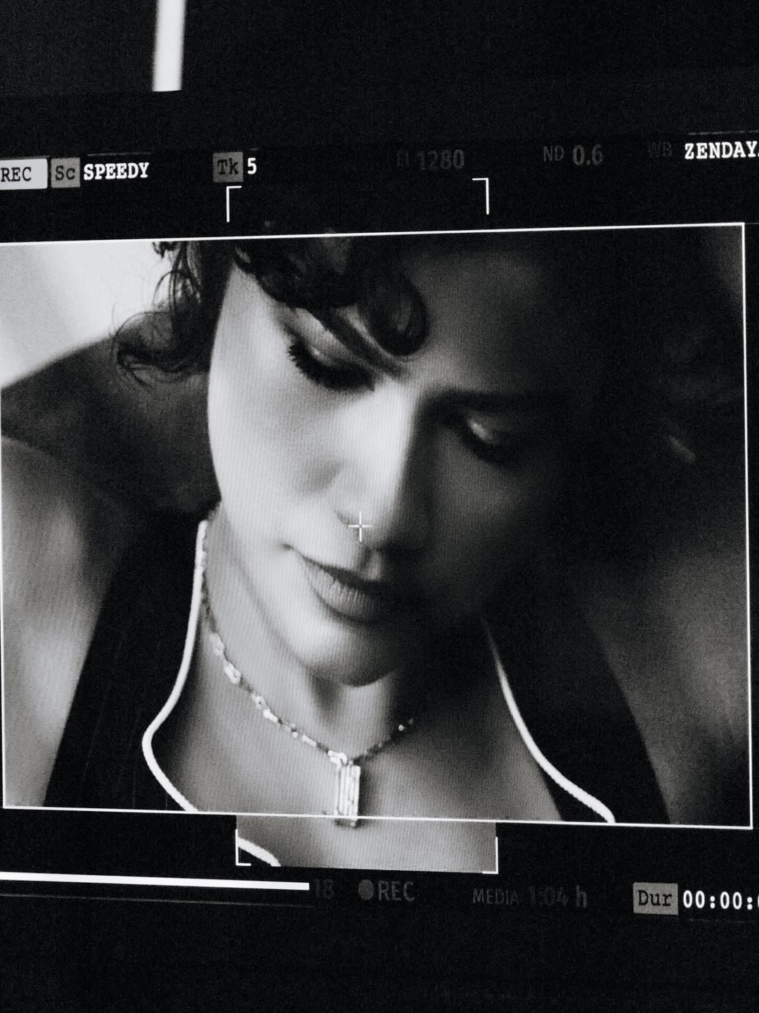 Black and white close-up of a woman with short dark hair wearing a necklace, with technical film details overlaid on the screen.