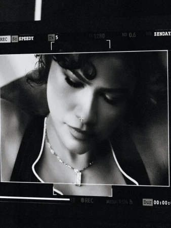 Black and white close-up of a woman with short dark hair wearing a necklace, with technical film details overlaid on the screen.