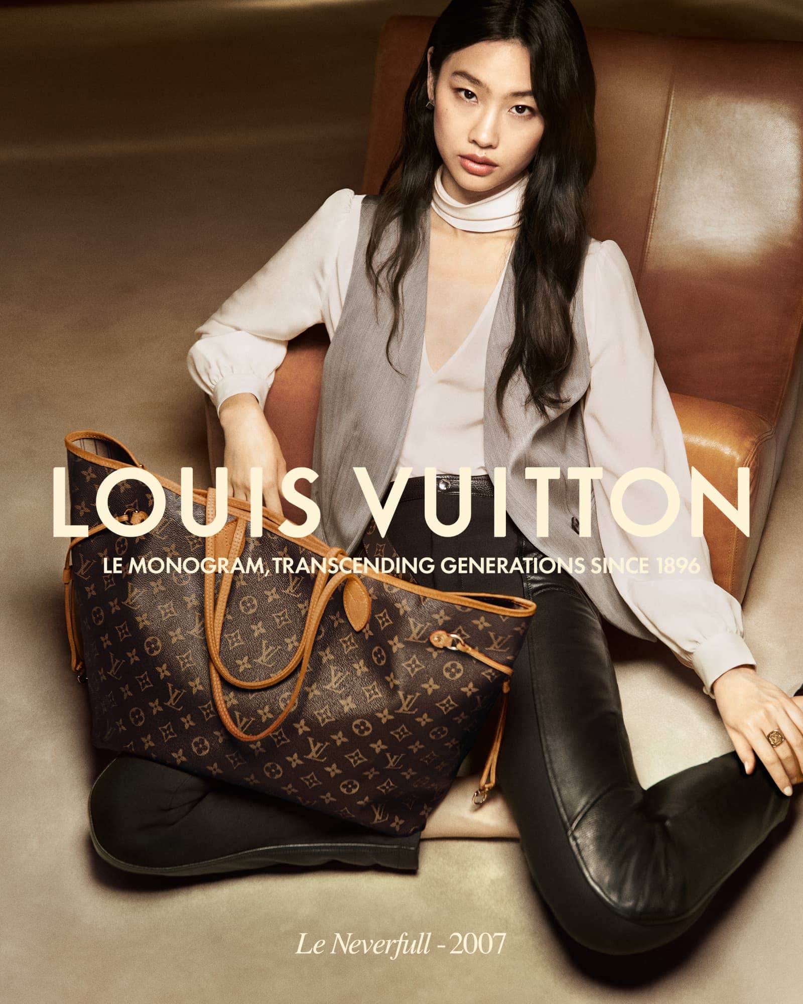 Woman sits with a Louis Vuitton bag in a fashion advertisement. Leather leggings, vest, and warm lighting create a stylish scene.