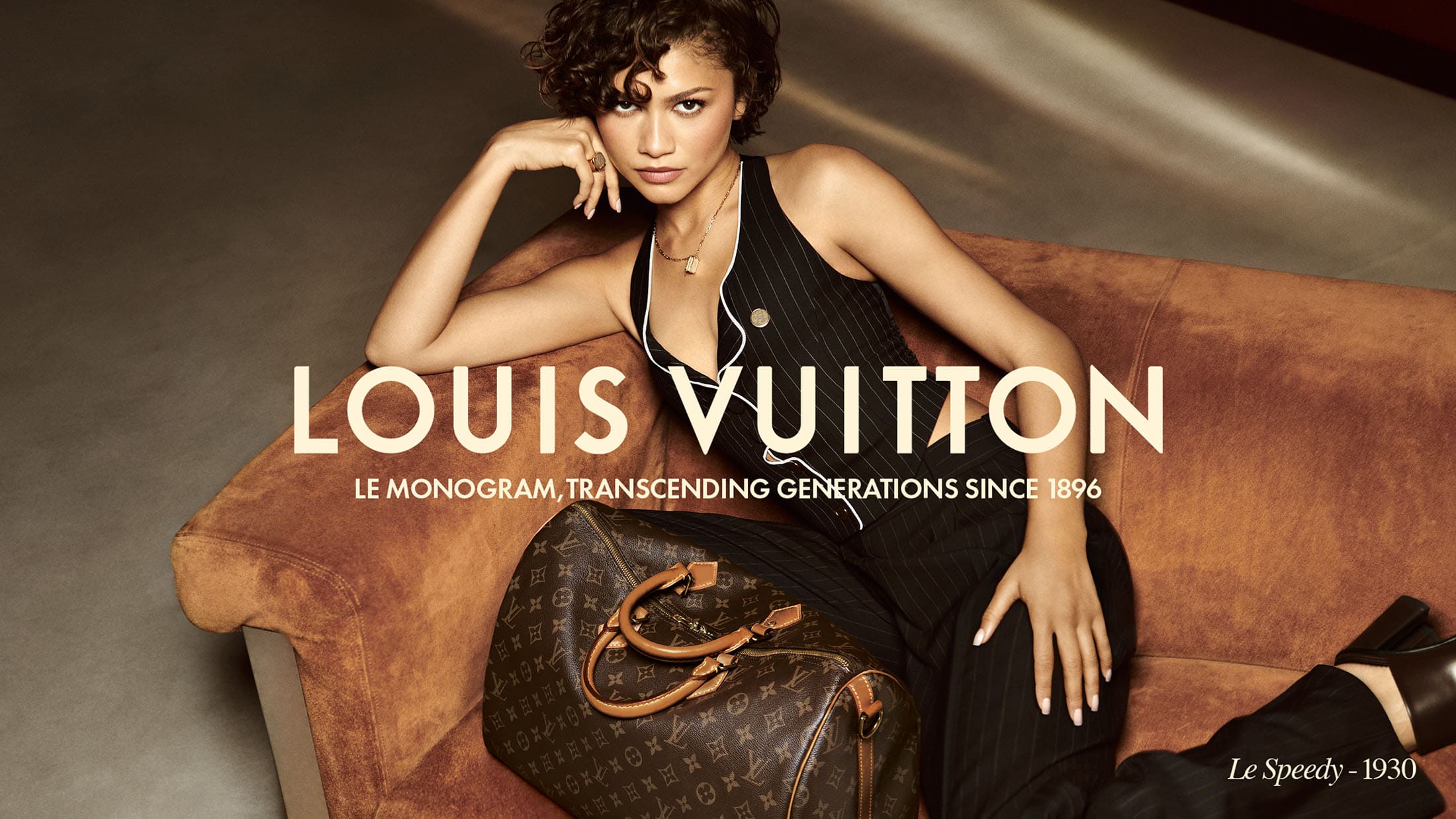 Zendaya poses with a Louis Vuitton handbag on a brown couch in a studio setting, capturing a blend of luxury and style.