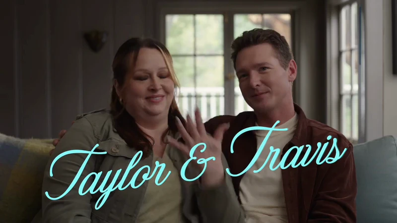 Indoor portrait of an adult male and adult female, smiling and waving in a living room with neutral-toned wall and window.