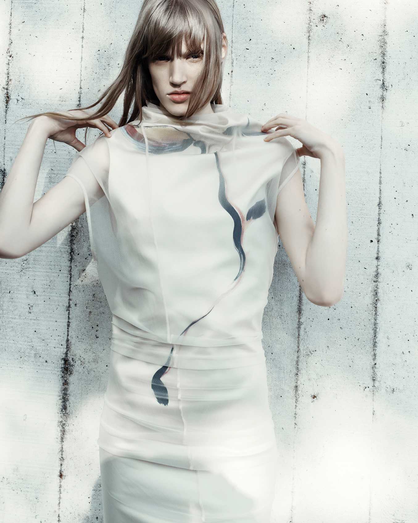 Model wearing a translucent white top with abstract dark brushstroke details against a concrete wall