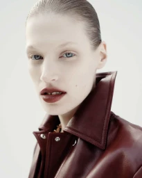 Close-up portrait of a woman wearing a dark red leather jacket against a white background for Sportmax.