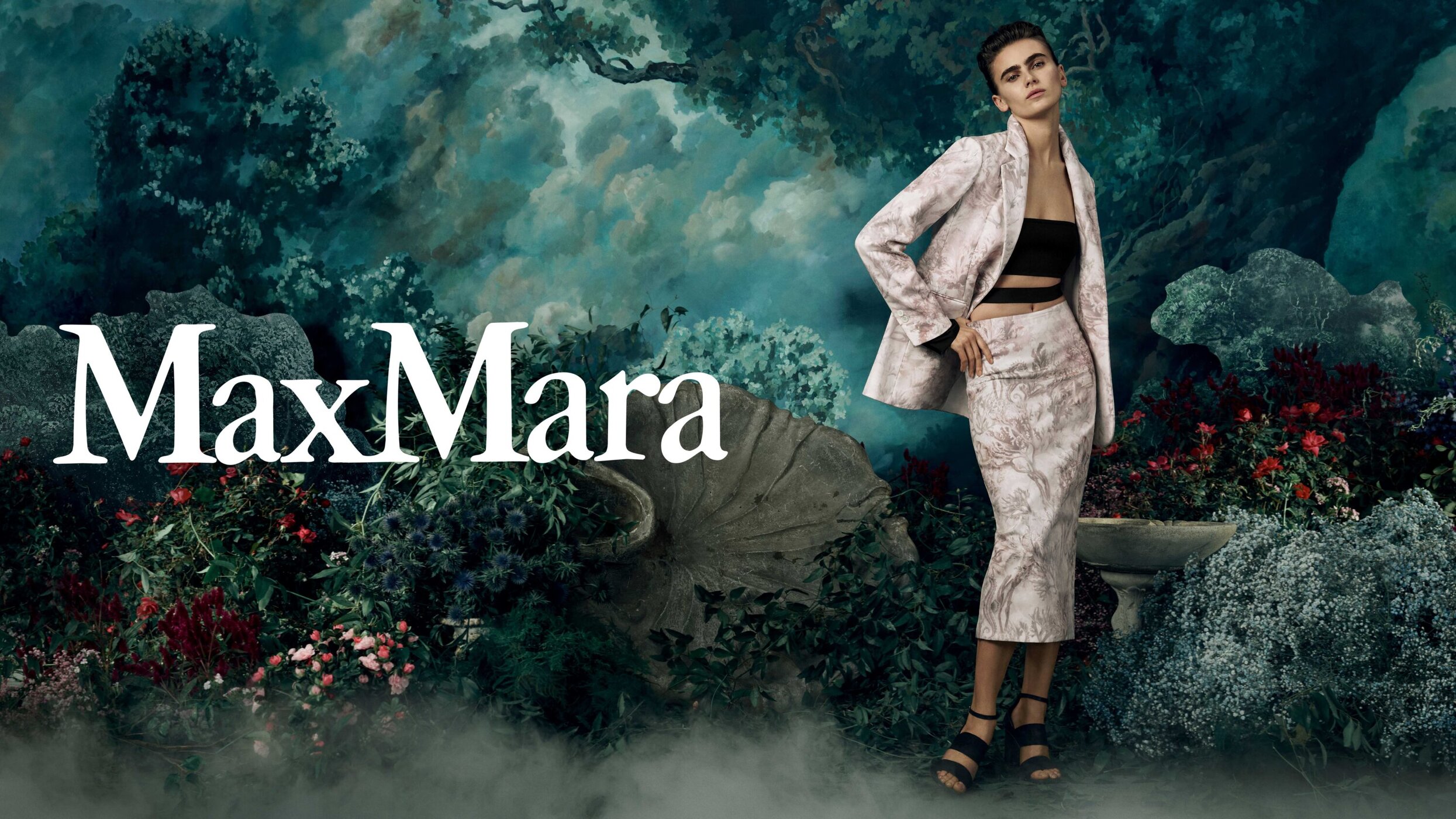 Max Mara campaign featuring a female model in a patterned skirt suit, posing against a dreamy backdrop of foliage and cloudy skies.