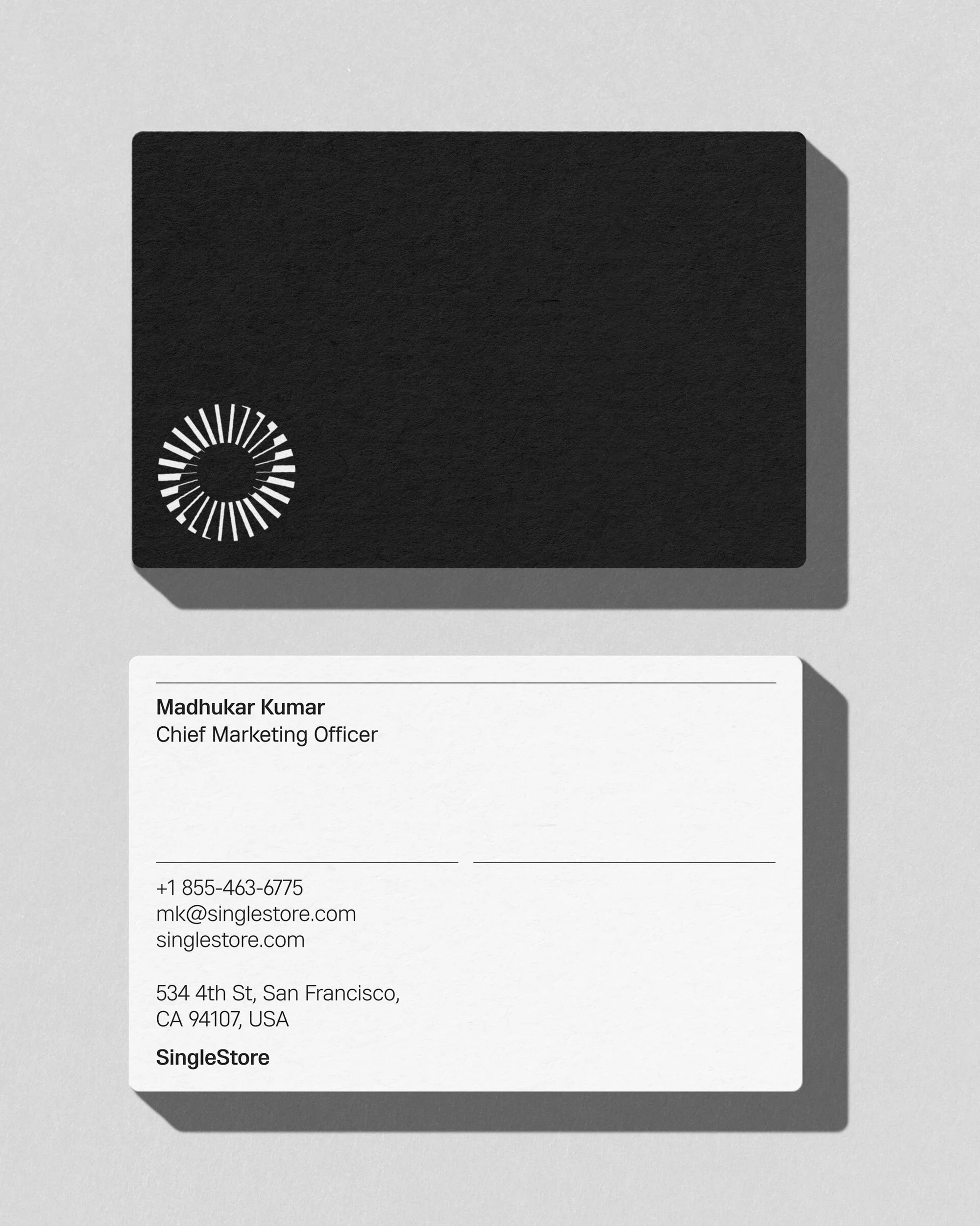 Two business cards, one black with a circular logo and one white with contact info, are displayed on a neutral background.