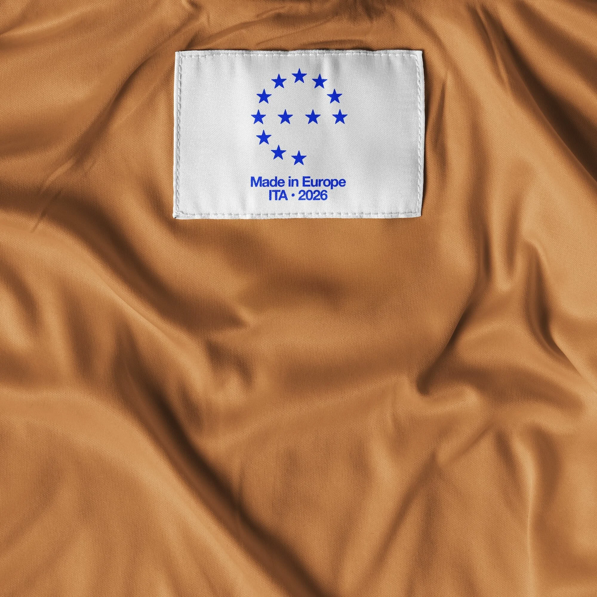Close-up of a white fabric tag with blue text and stars sewn onto a brown, shiny, crinkled fabric, possibly the lining of a garment.