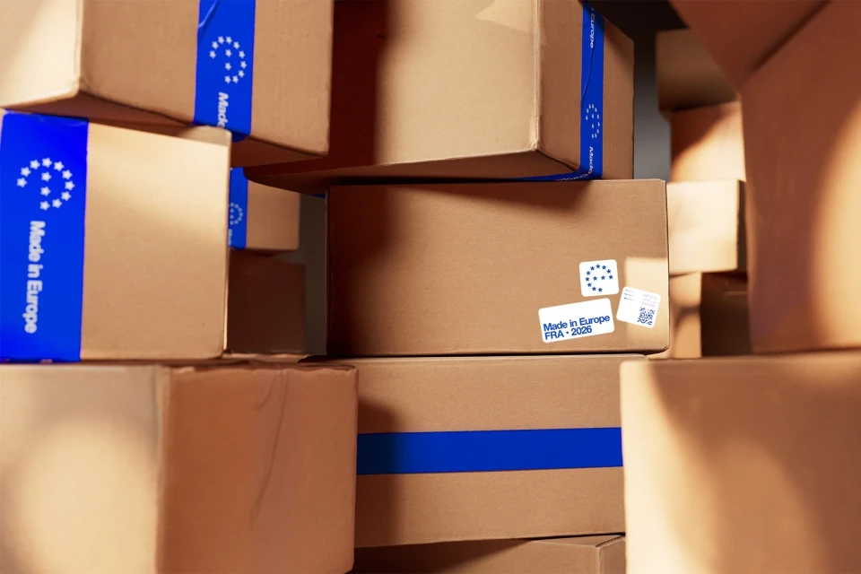 Stacked brown cardboard shipping boxes with blue stripes and 'Made in Europe' labels, conveying logistics and EU manufacturing.