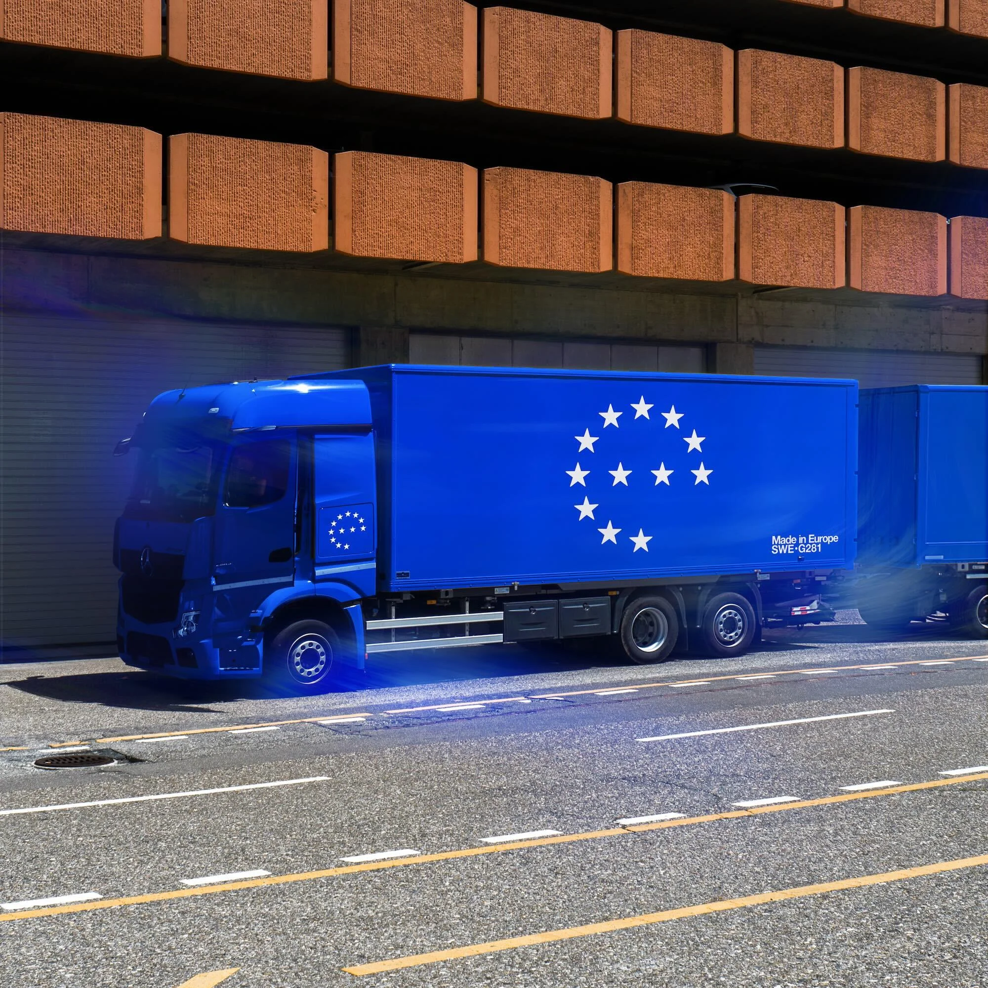 Blue tractor trailer with European Union flag parked on city street against brick building for logistics, transportation or international trade.