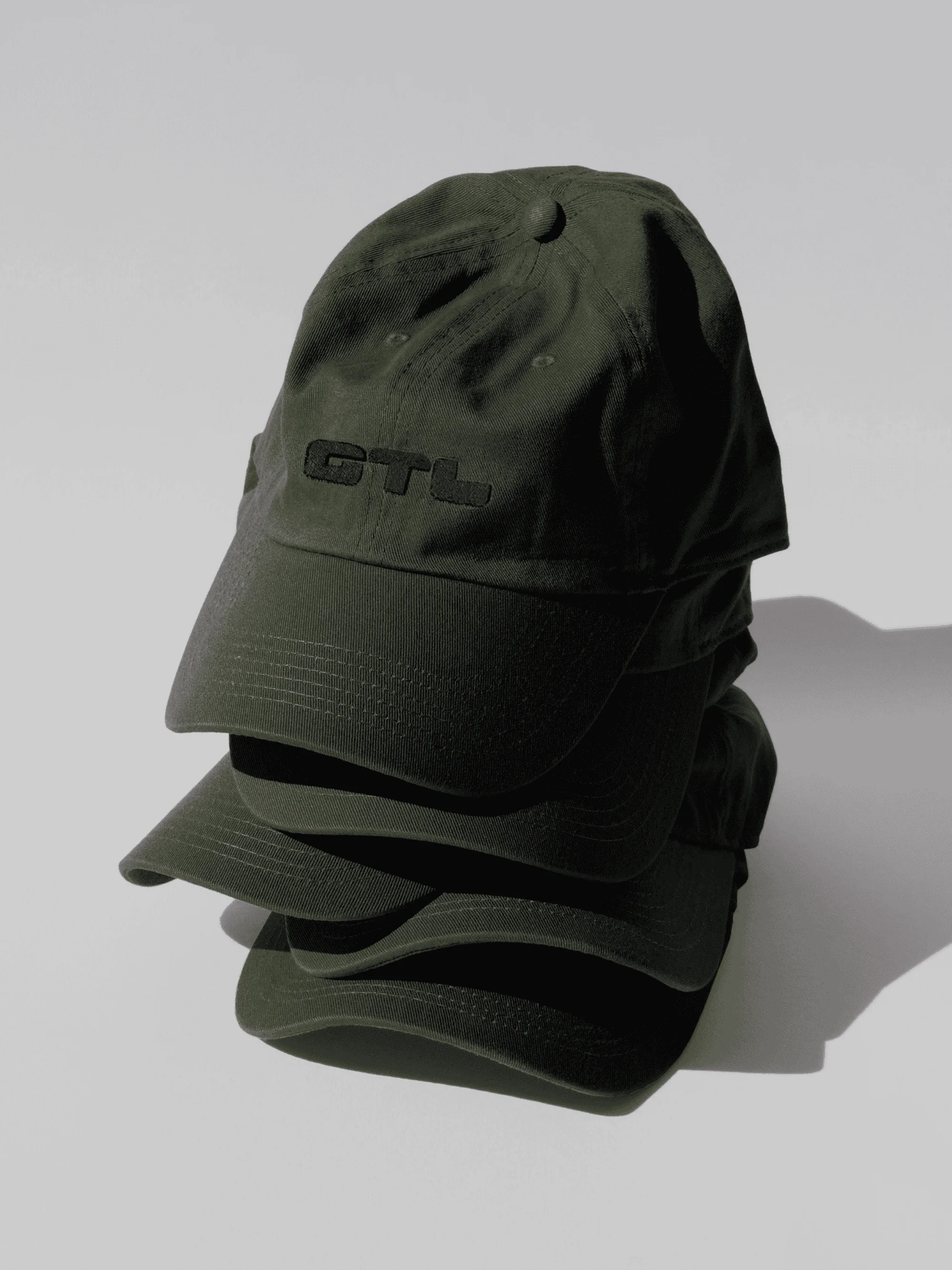 Stack of dark green baseball caps with GTL logo on white background in product photography-style, studio lighting, clean and simple.