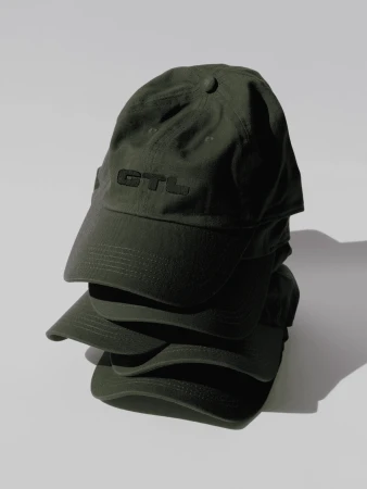 Stack of dark green baseball caps with GTL logo on white background in product photography-style, studio lighting, clean and simple.