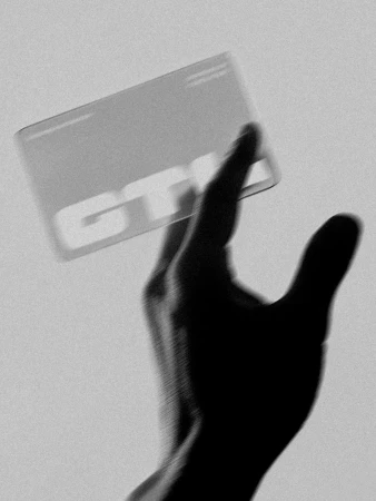 Monochromatic shot of a silhouetted hand holding a translucent credit card with the letters 'GTK' in a dimly lit setting.