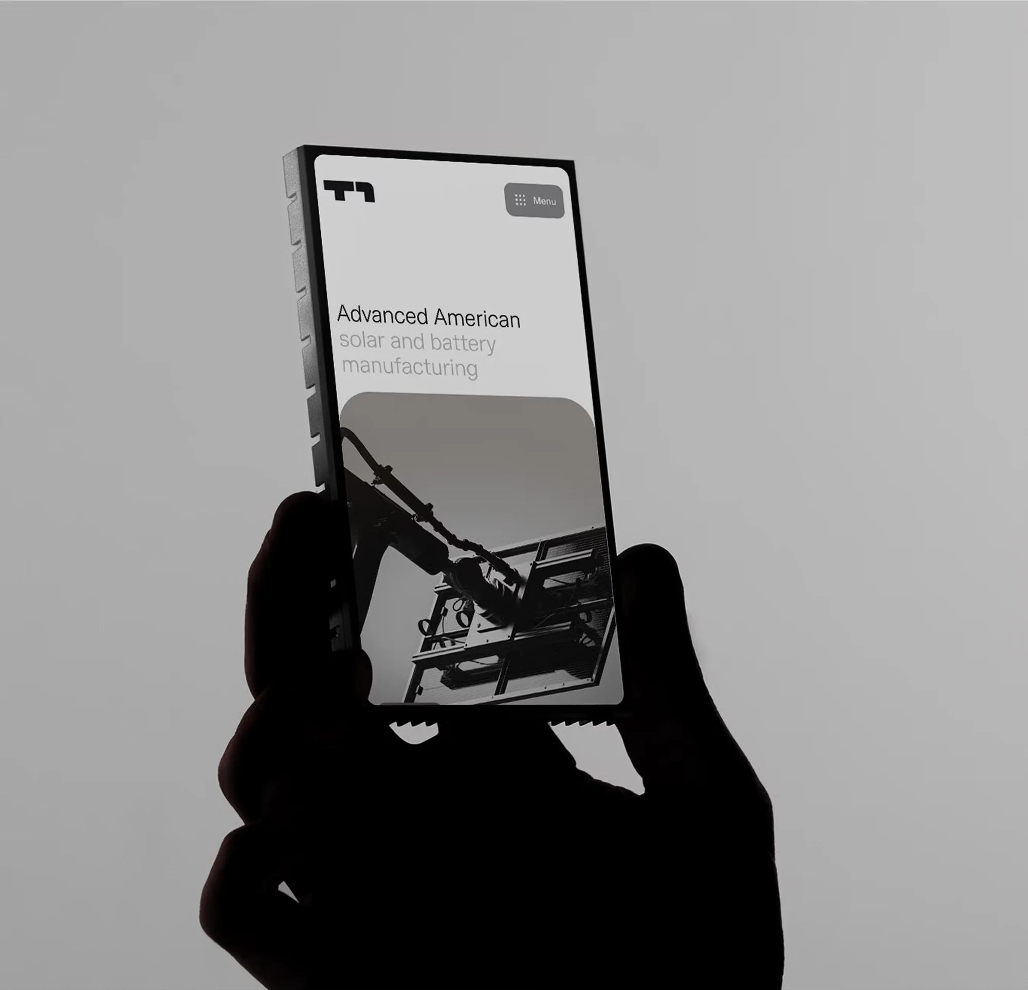 Close-up of a hand holding a smartphone displaying an image of a tower crane and the text 'Advanced American solar and battery manufacturing'.