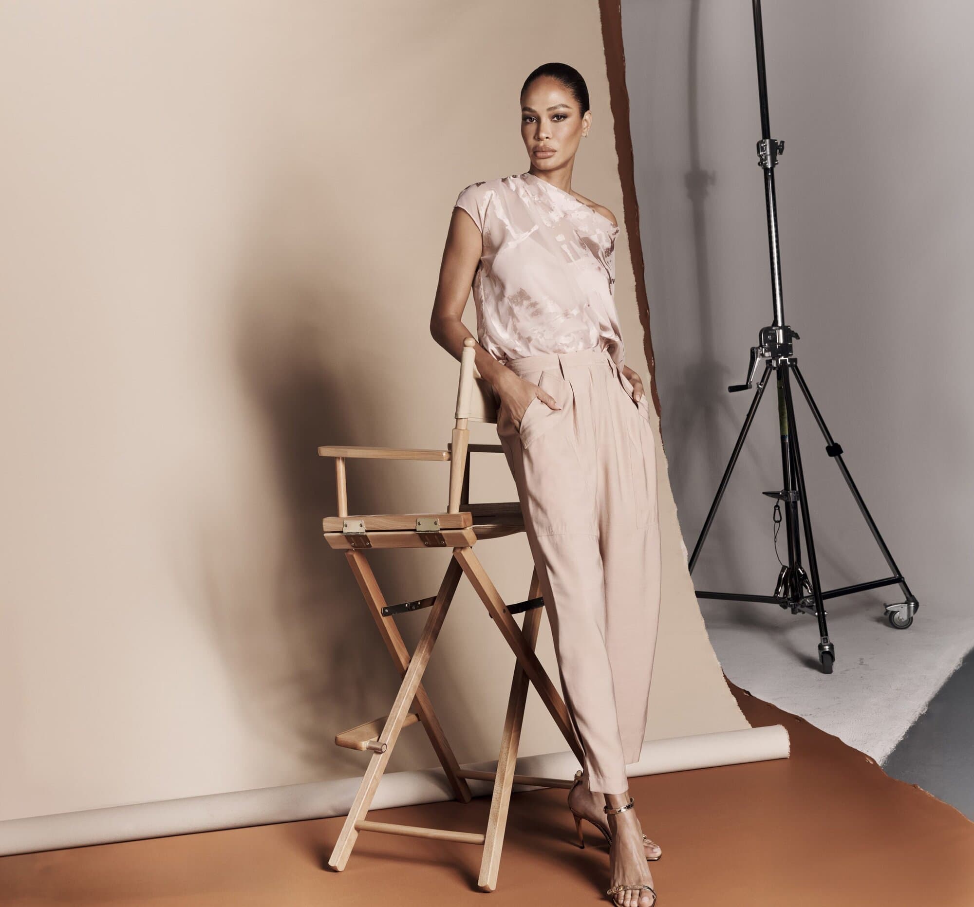 Elegant woman in stylish outfit poses in a studio with a director's chair and lighting equipment, showcasing fashion and photographic artistry.