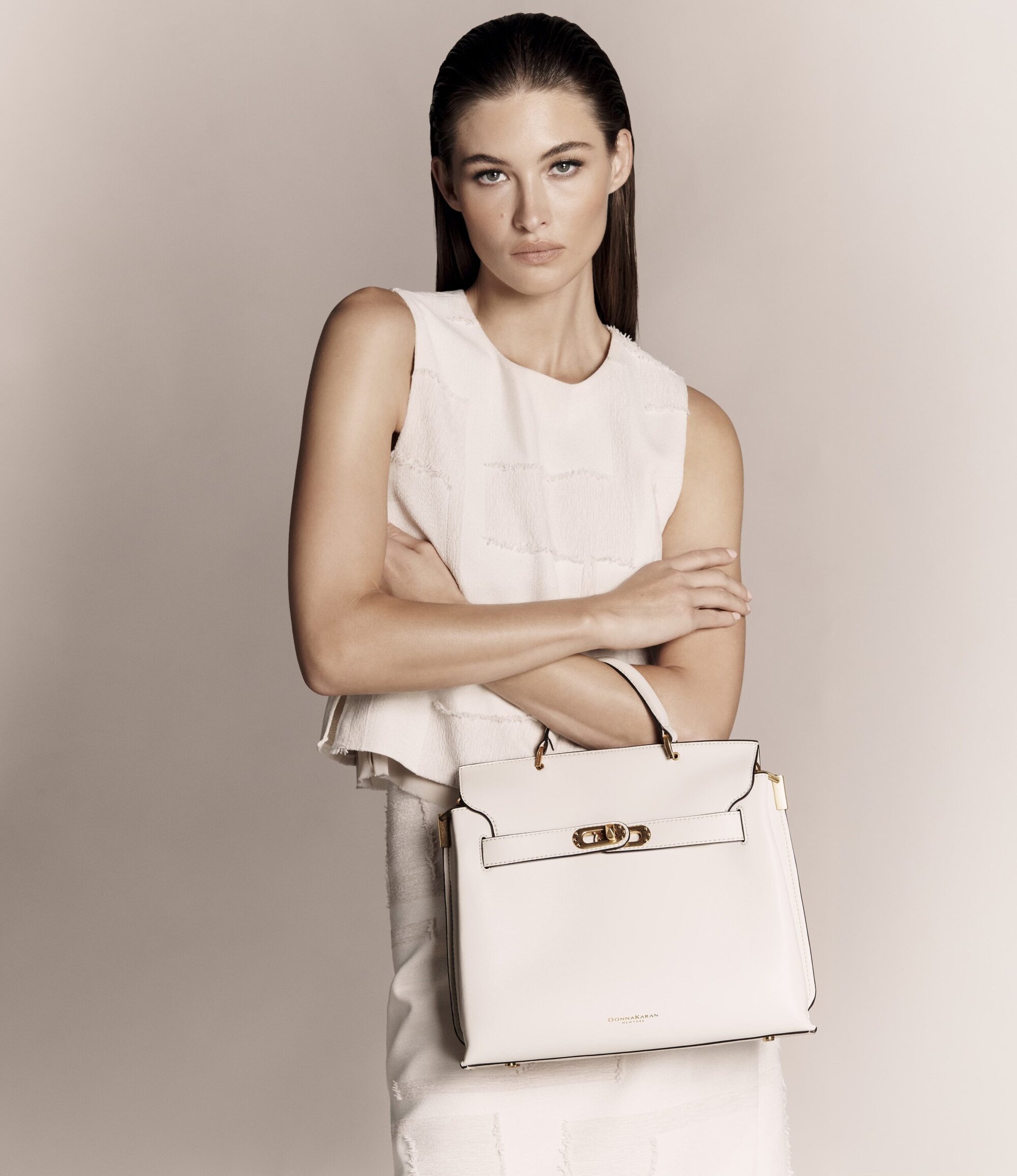 Woman with handbag in a studio shot. Female model in a white sleeveless shirt poses with a matching white handbag in a studio setting.
