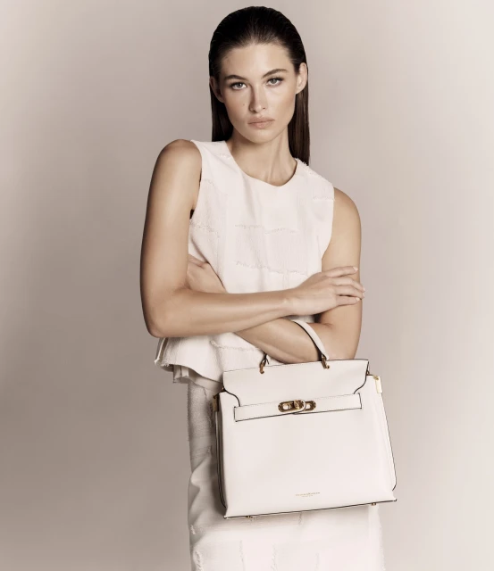 Woman with handbag in a studio shot. Female model in a white sleeveless shirt poses with a matching white handbag in a studio setting.
